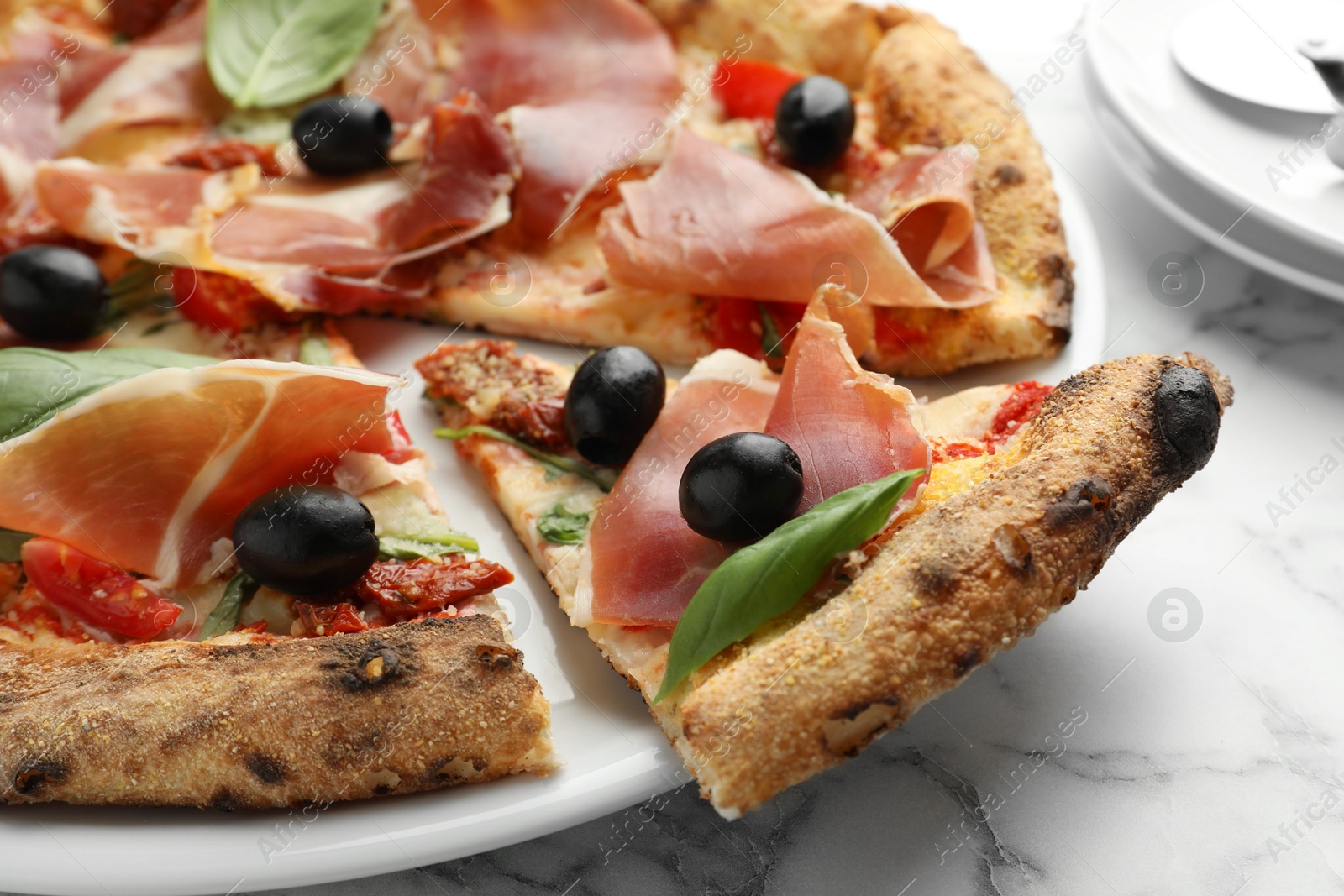 Photo of Tasty pizza with cured ham, olives, sun-dried tomato and basil on white table, closeup