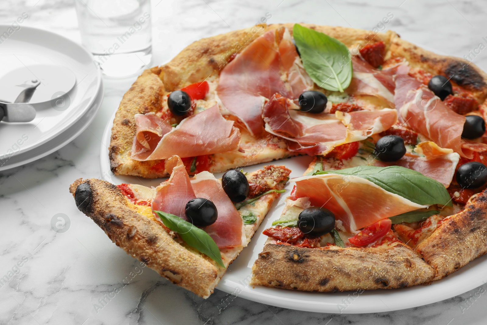 Photo of Tasty pizza with cured ham, olives, sun-dried tomato and basil on white table, closeup