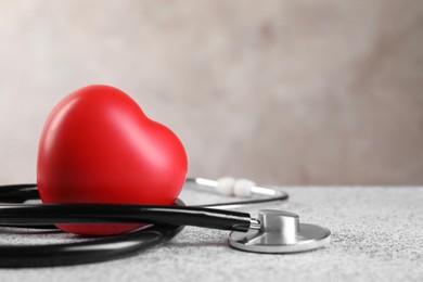 Photo of Stethoscope and red heart on grey stone table, closeup. Space for text