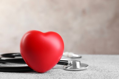 Photo of Stethoscope and red heart on grey stone table. Space for text