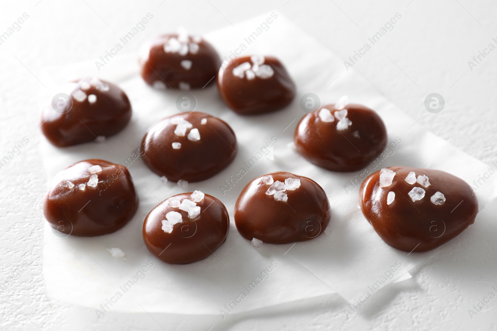 Photo of Tasty caramel candies and salt on white table, closeup