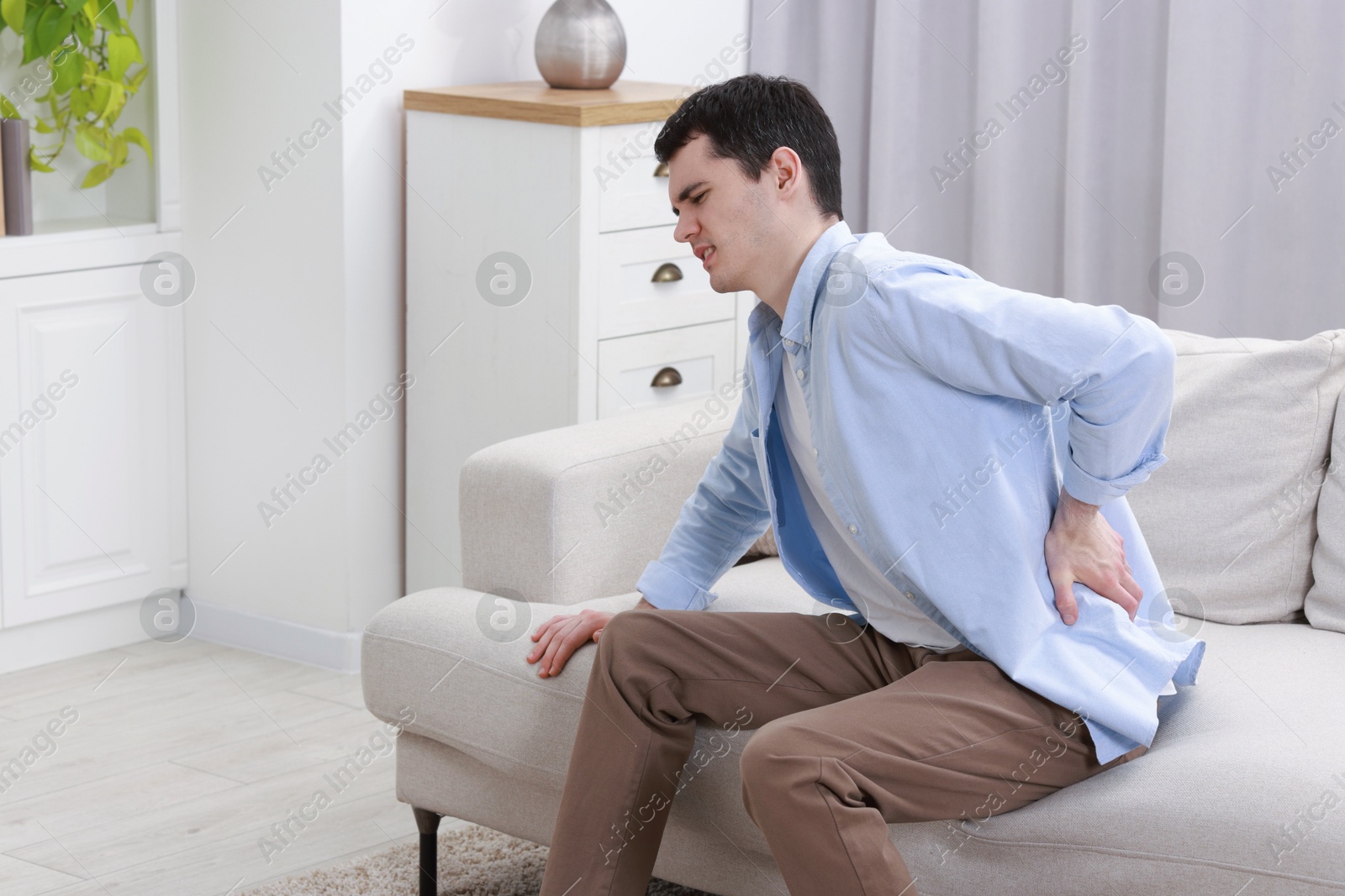Photo of Man suffering from back pain on sofa indoors