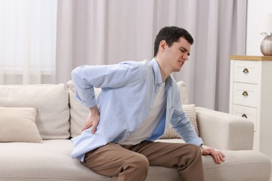 Photo of Man suffering from back pain on sofa indoors