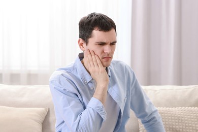 Man suffering from toothache on sofa at home