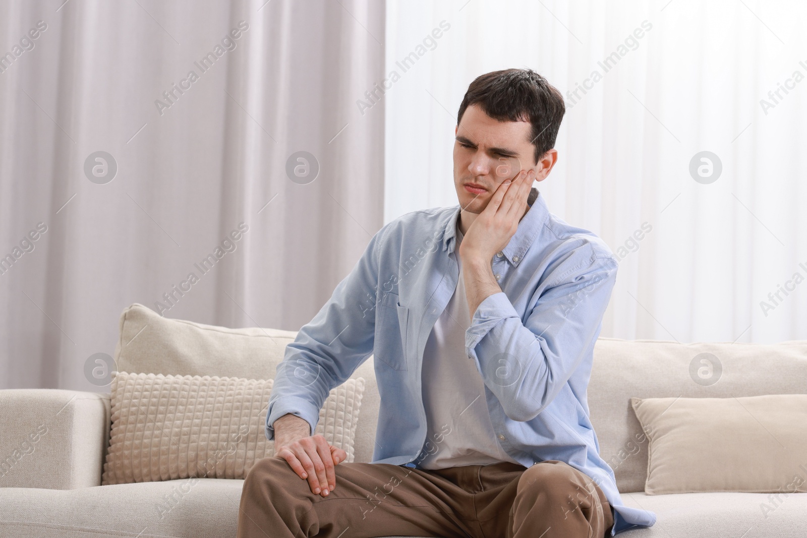 Photo of Man suffering from toothache on sofa at home