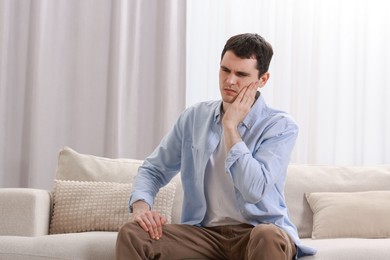 Photo of Man suffering from toothache on sofa at home