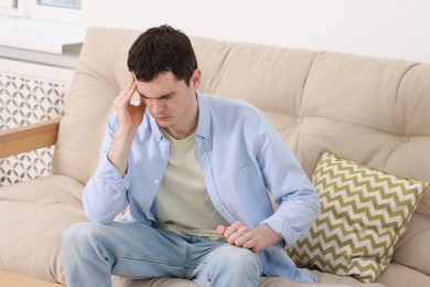 Photo of Man suffering from headache on sofa at home