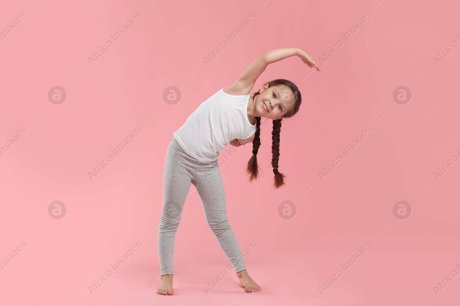 Photo of Cute little girl stretching on pink background