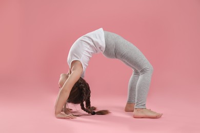 Photo of Cute little girl doing gymnastic exercise on pink background