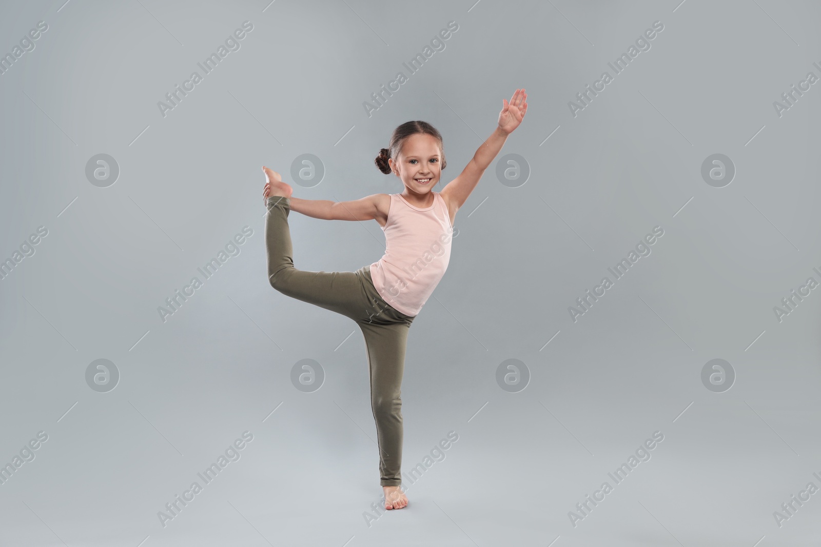 Photo of Cute little girl stretching on grey background