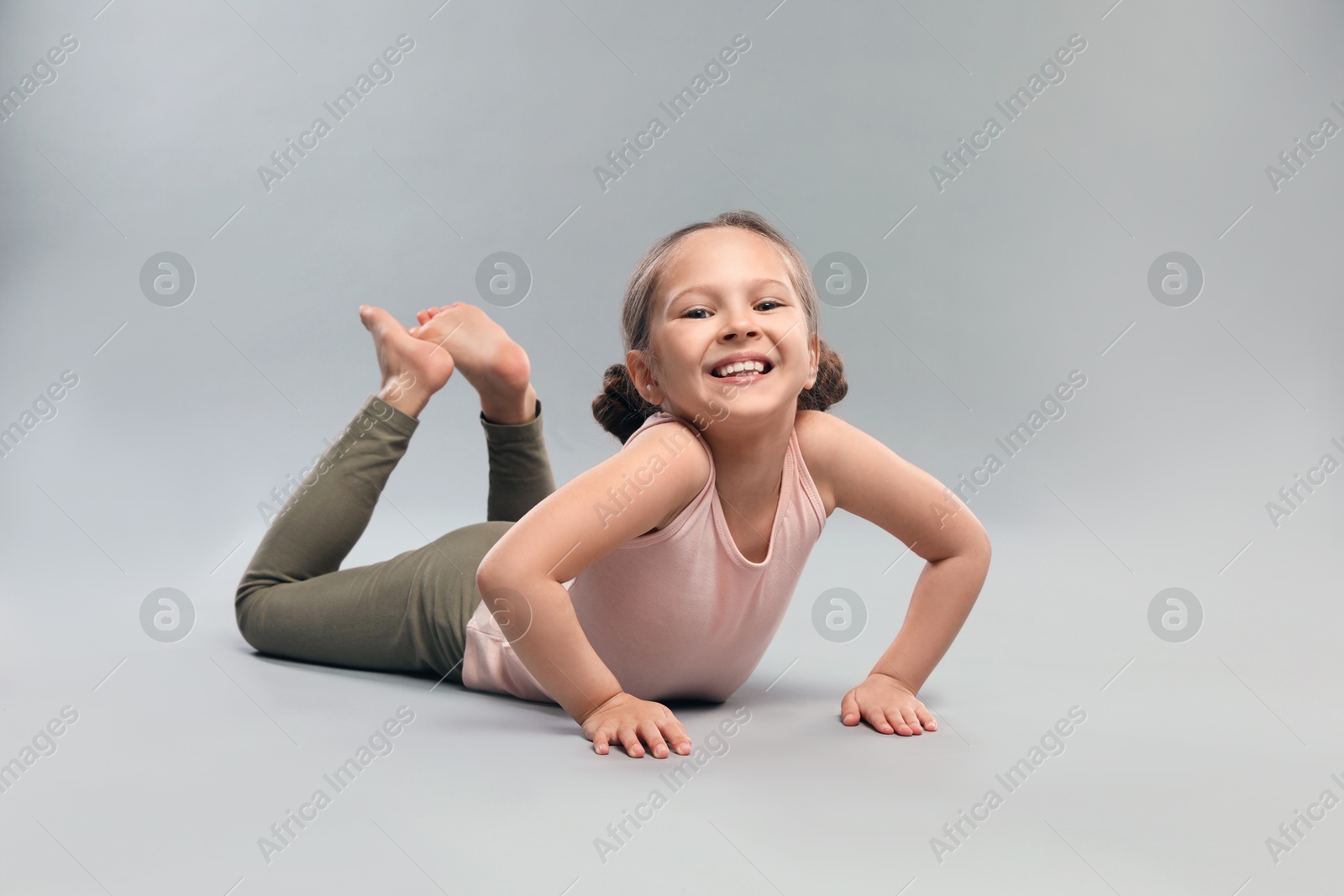 Photo of Cute little girl doing gymnastic exercise on grey background