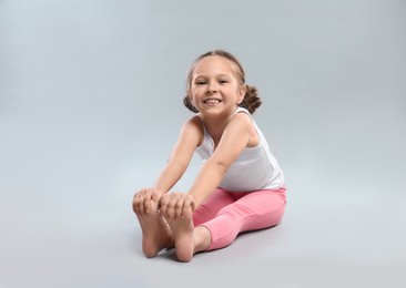 Photo of Cute little girl stretching on grey background