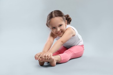 Photo of Cute little girl stretching on grey background