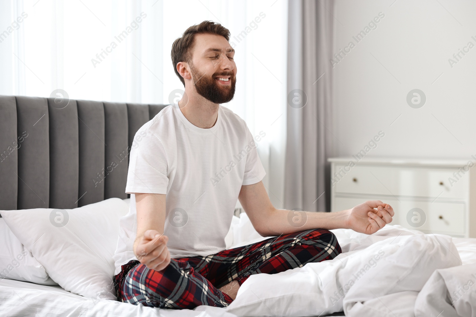 Photo of Happy young man meditating on bed at morning