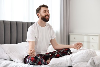 Happy young man meditating on bed at morning