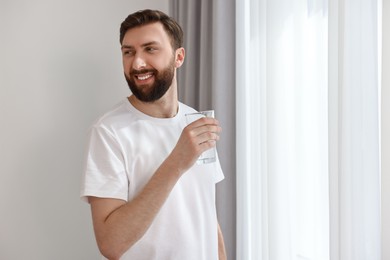 Photo of Happy young man with glass of water near window at morning