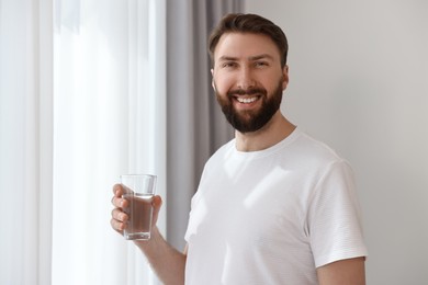 Happy young man with glass of water near window at morning