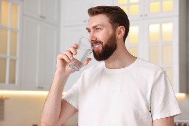 Photo of Happy young man with glass of water in kitchen at morning