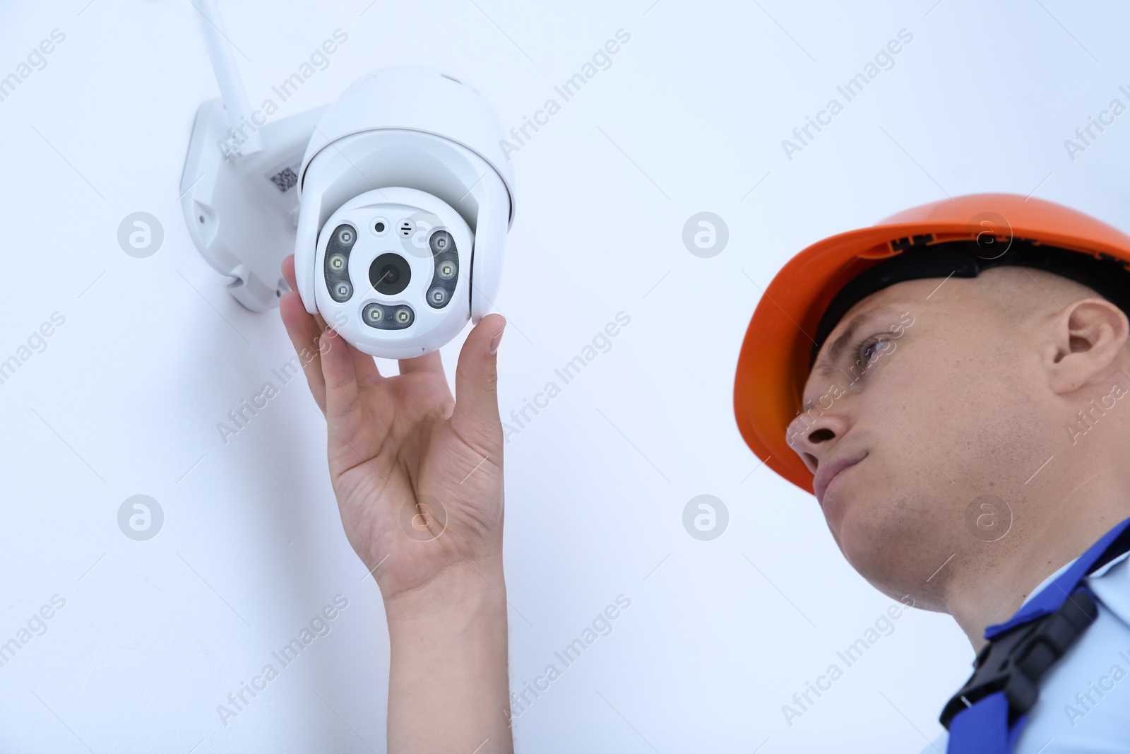 Photo of Technician installing CCTV camera on wall indoors, low angle view