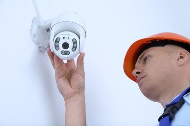 Technician installing CCTV camera on wall indoors, low angle view