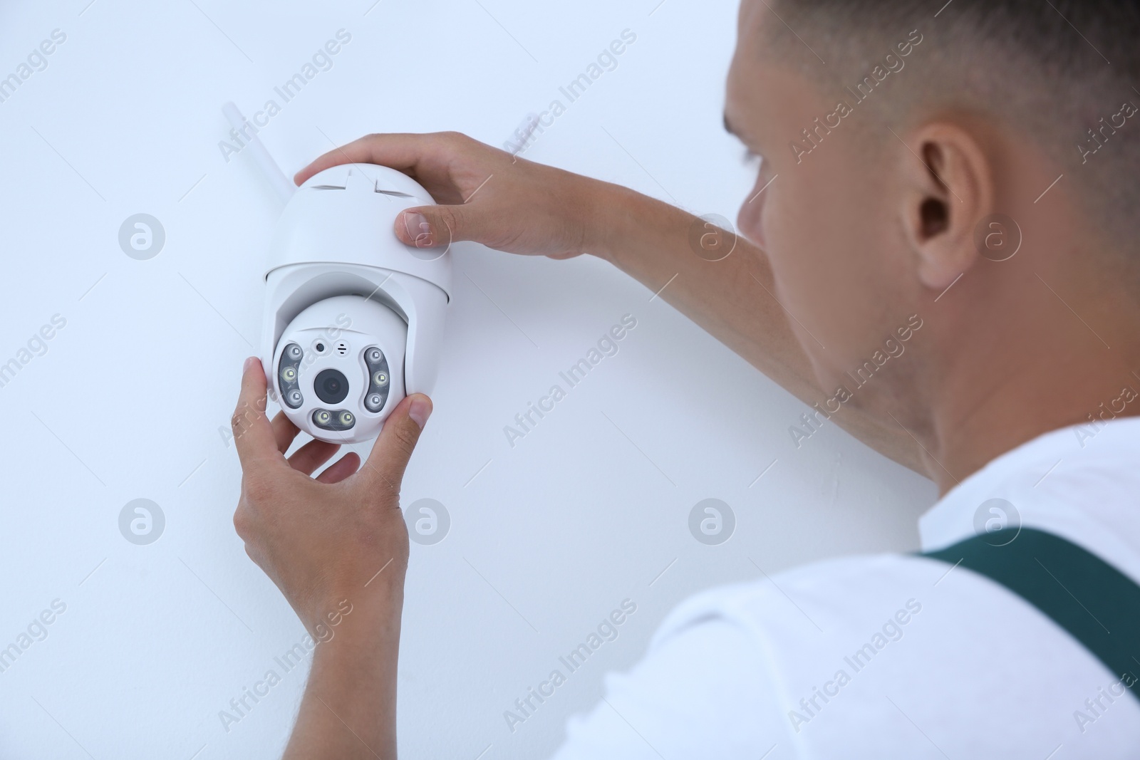 Photo of Technician installing CCTV camera on wall indoors, closeup