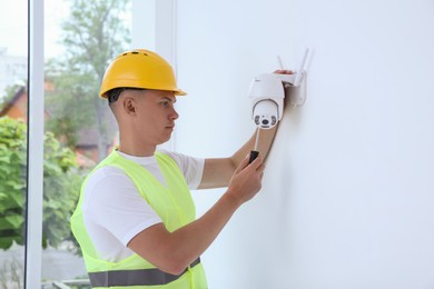 Technician with screwdriver installing CCTV camera on wall indoors