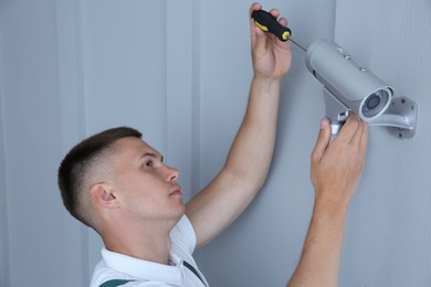 Photo of Technician with screwdriver installing CCTV camera on wall indoors