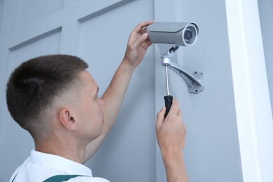 Technician with screwdriver installing CCTV camera on wall indoors