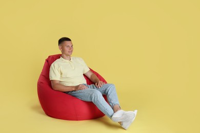 Photo of Handsome man sitting on red bean bag chair against yellow background. Space for text