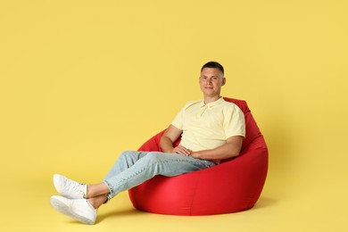 Photo of Handsome man sitting on red bean bag chair against yellow background. Space for text