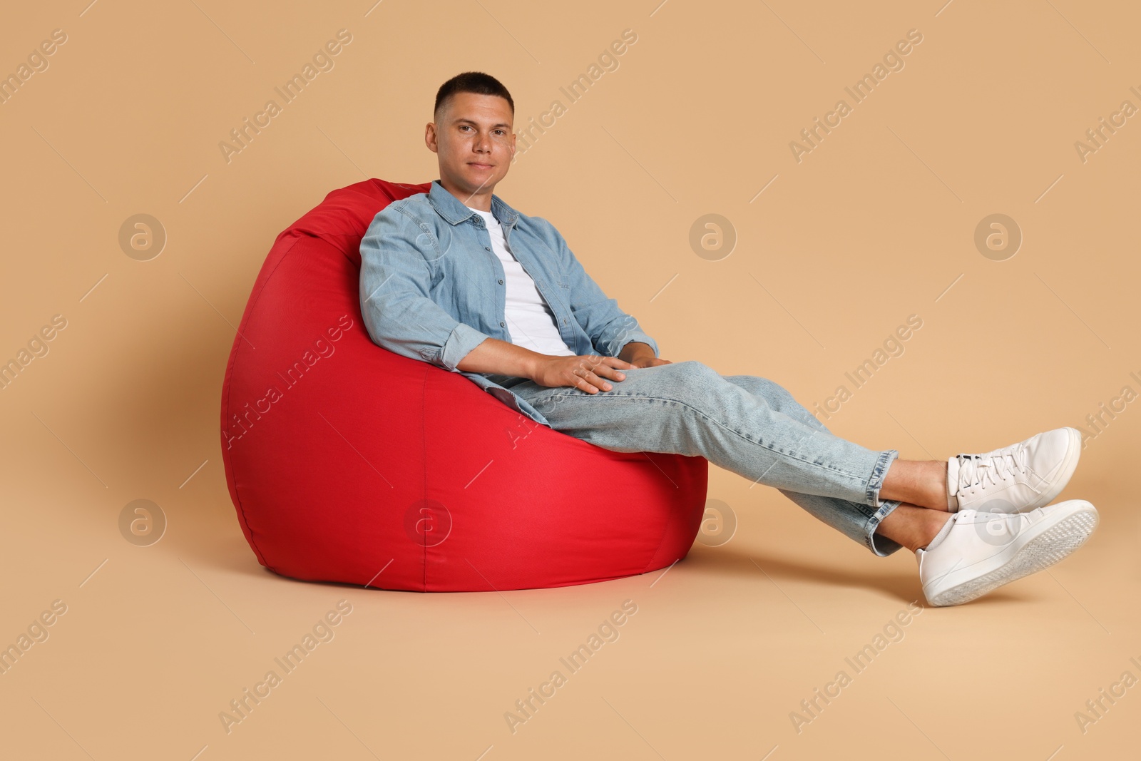 Photo of Handsome man on red bean bag chair against beige background