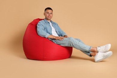 Photo of Handsome man on red bean bag chair against beige background
