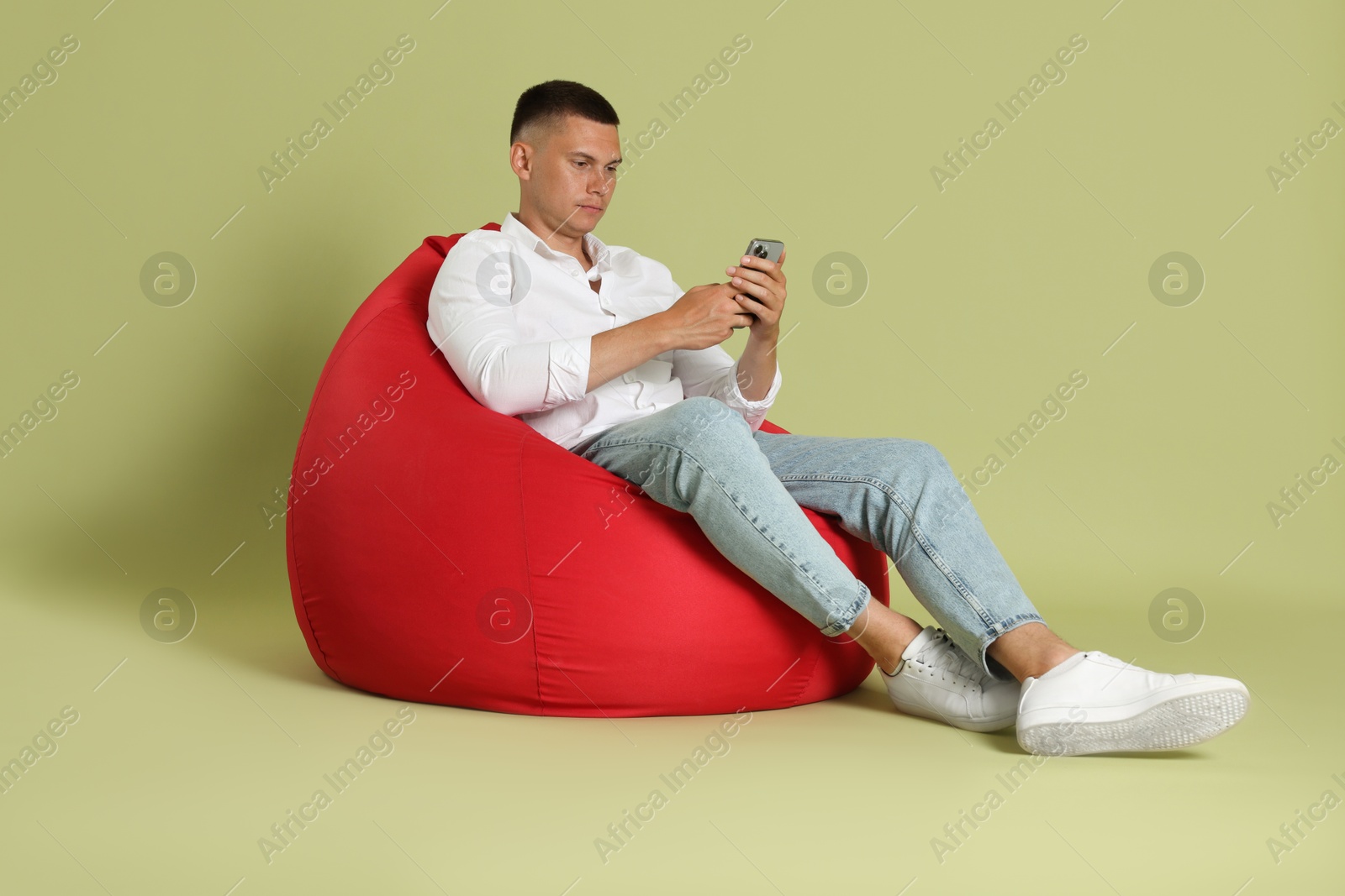 Photo of Handsome man with smartphone on red bean bag chair against green background