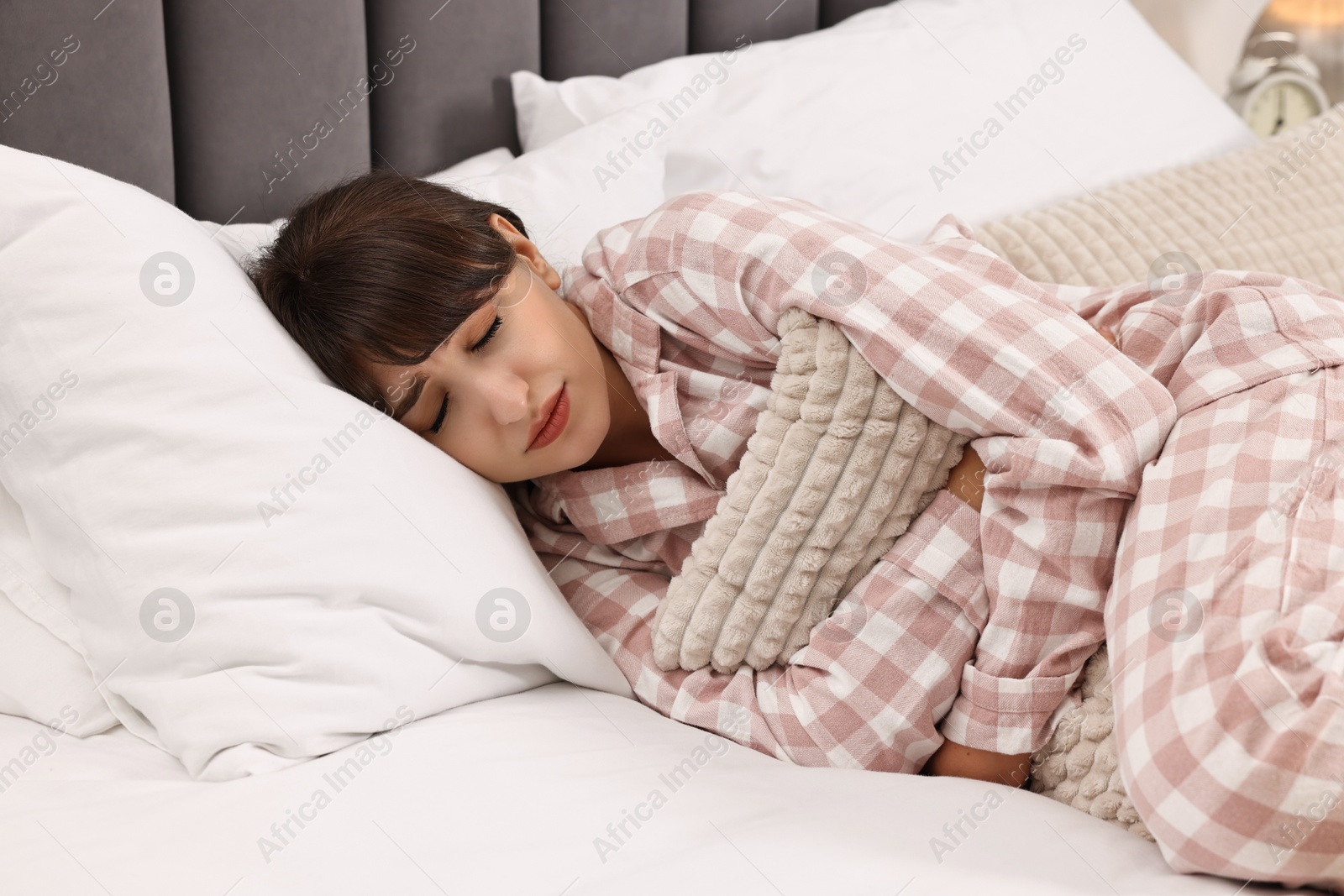 Photo of Upset woman with pillow suffering from abdominal pain on bed at home