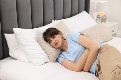 Photo of Upset woman suffering from abdominal pain on bed at home