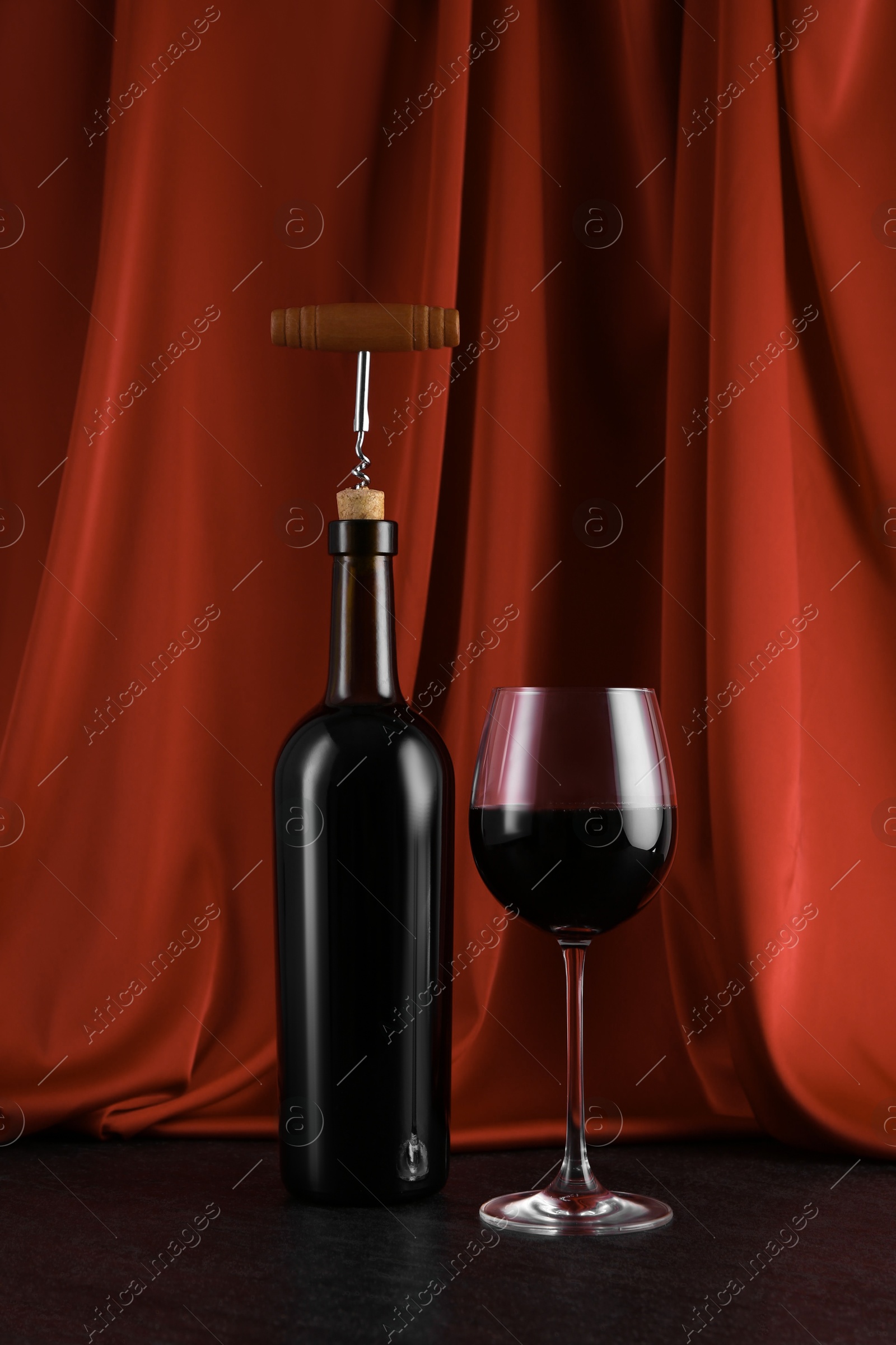 Photo of Corkscrew, glass of wine and bottle on black table