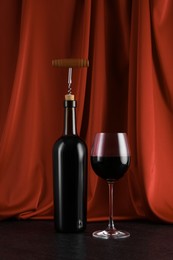 Corkscrew, glass of wine and bottle on black table