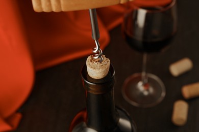 Photo of Wine bottle with corkscrew, glass and corks on table, closeup