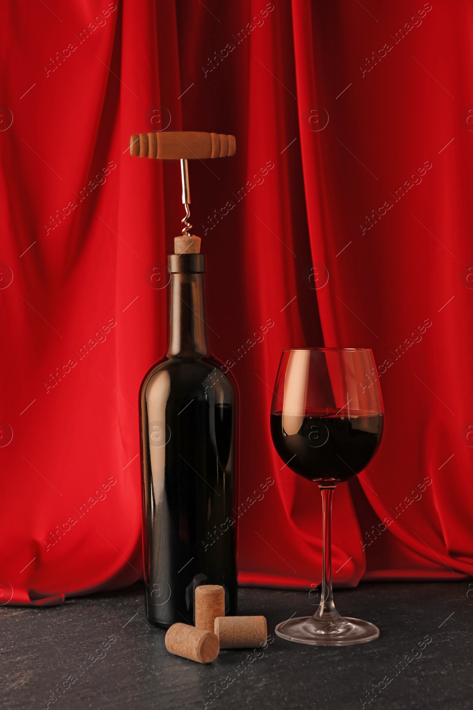 Photo of Corkscrew, glass of wine, bottle and corks on black table