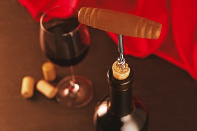 Photo of Wine bottle with corkscrew, glass and corks on table, closeup