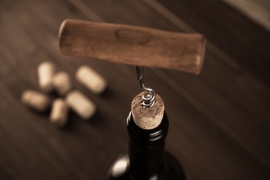 Wine bottle with corkscrew on wooden table, closeup