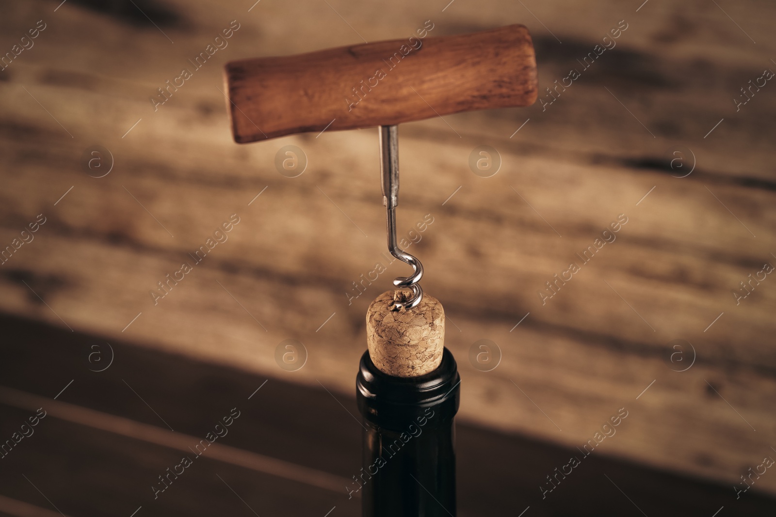 Photo of Wine bottle with corkscrew on wooden background, closeup