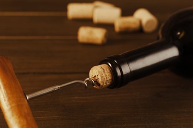 Wine bottle with corkscrew on wooden table, closeup