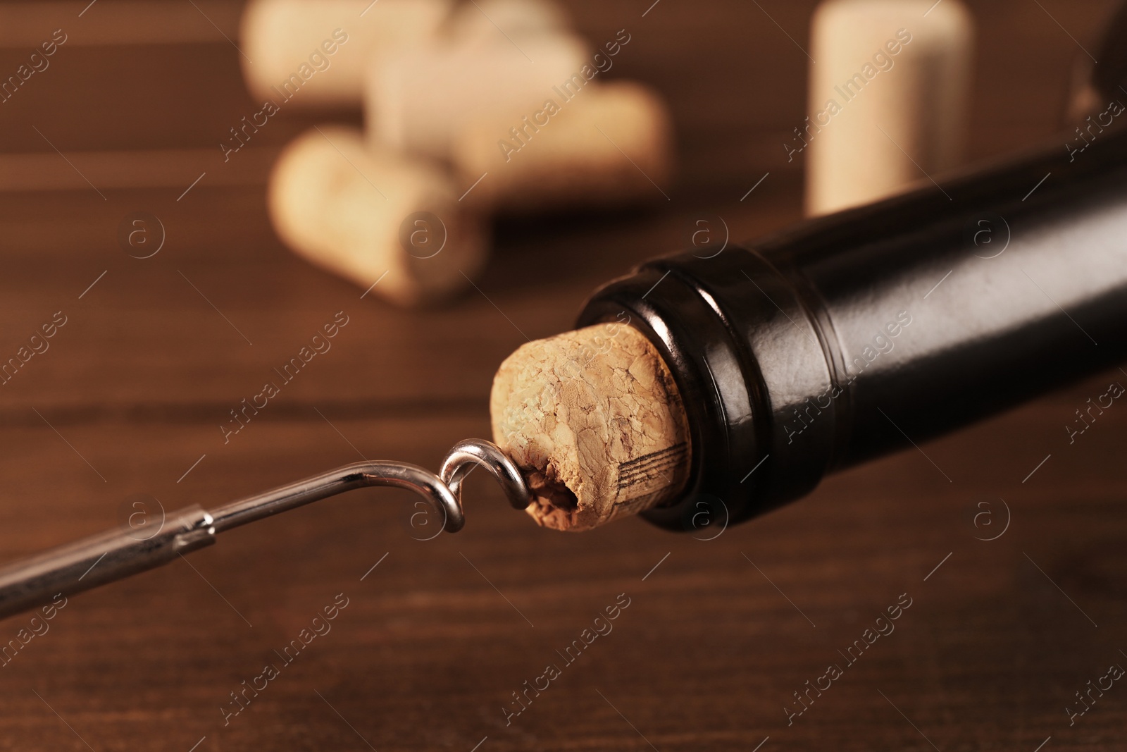 Photo of Wine bottle with corkscrew on wooden table, closeup