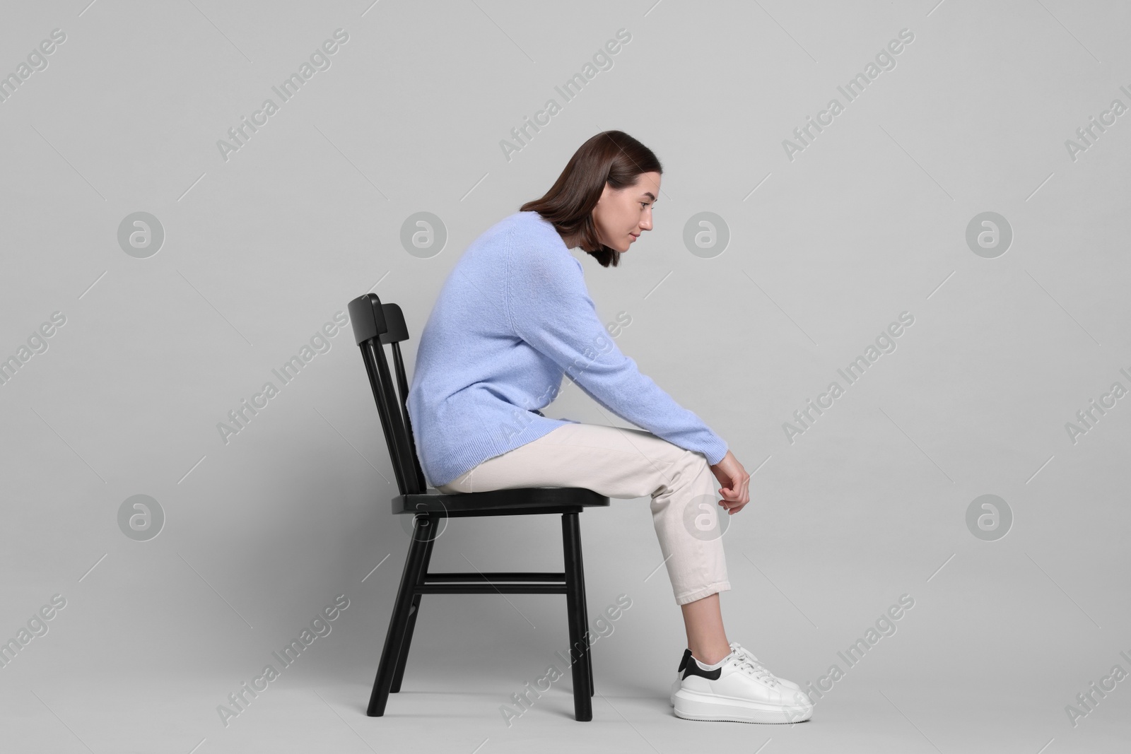 Photo of Woman with poor posture sitting on chair against gray background