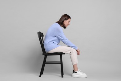 Woman with poor posture sitting on chair against gray background