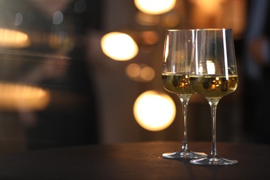 Photo of Tasty wine in glasses on black table against blurred lights, space for text