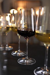 Photo of Different tasty wines in glasses on black table against blurred lights, closeup