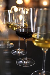 Different tasty wines in glasses on black table against blurred lights, closeup