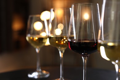 Photo of Different tasty wines in glasses on table against blurred lights, closeup